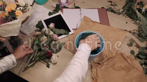男性花艺师在木制桌子上的花店里制作花束手上可以看到鲜花平板玫瑰和装饰视频的预览图