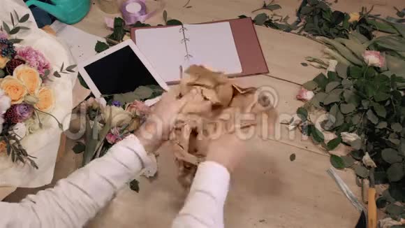 男性花艺师在木制桌子上的花店里制作花束手上可以看到鲜花平板玫瑰和装饰视频的预览图