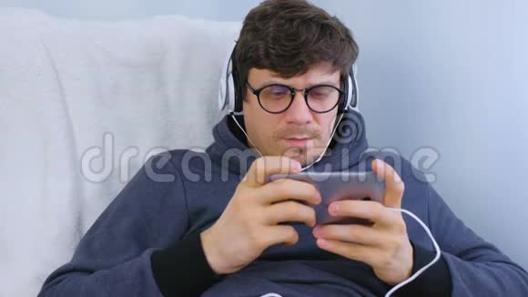 戴着眼镜和耳机的人在智能手机里玩游戏玩家放松视频的预览图