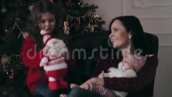 在圣诞树旁有新生婴儿和女儿的年轻母亲视频的预览图
