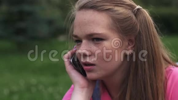 一个长着雀斑的年轻漂亮女孩会打电话夏日公园肖像视频的预览图