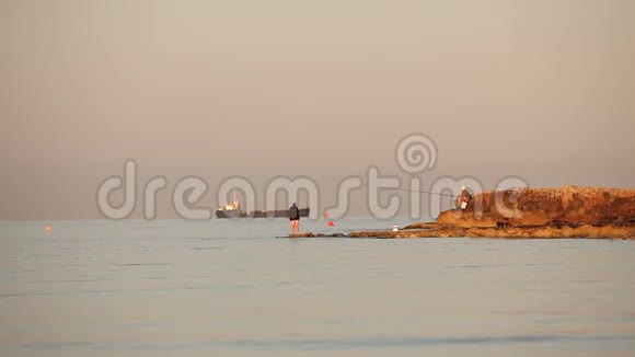 一个渔夫在黎明的海面上捕鱼一个渔夫在黎明的天空下在岩石上捕鱼一群渔夫和一群剪影视频的预览图