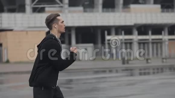 有魅力的年轻人在户外跑步戴着耳机动作缓慢雨天心脏锻炼健康视频的预览图