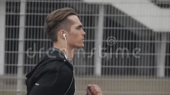 有魅力的年轻人在户外跑步戴着耳机动作缓慢雨天心脏锻炼健康视频的预览图
