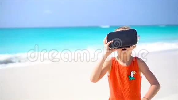 可爱的小女孩使用VR虚拟现实护目镜可爱的女孩看着白色海滩上的虚拟眼镜视频的预览图