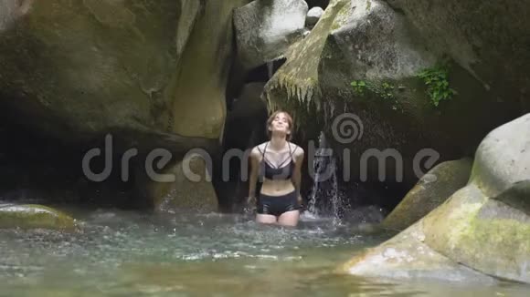 在绿色的热带森林里美丽的女孩用双手溅在水上小瀑布和视频的预览图