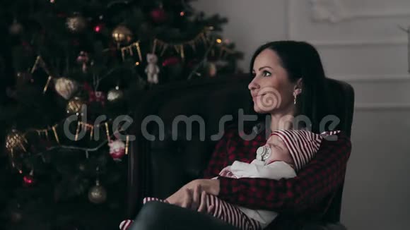 在圣诞树旁有新生婴儿和女儿的年轻母亲视频的预览图