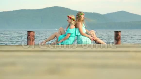 可爱的女孩头上戴着花环正在河上休息两个穿着蓝色裙子的年轻美女坐在视频的预览图