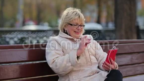 女人坐在路边的长凳上通过智能手机进行交流视频的预览图
