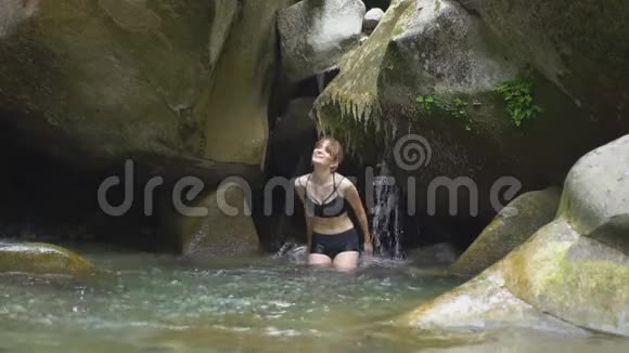 在绿色的热带森林中美丽的女孩用手在山上的湖水上溅起小瀑布视频的预览图