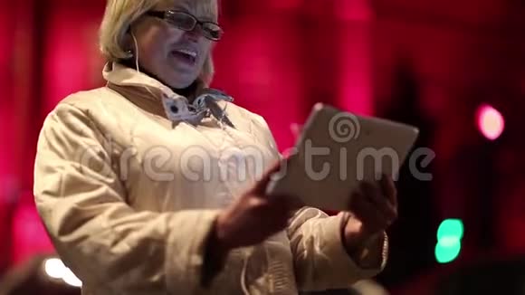 有平板电脑的老妇人在夜间站在道路和红色建筑附近视频的预览图