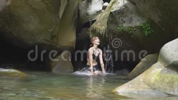 在绿色的热带森林中美丽的女孩用手在山上的湖上溅起水花上面有小瀑布视频的预览图