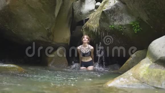 在绿色的热带森林中美丽的女孩用手在山间湖泊中溅起水花小瀑布和视频的预览图