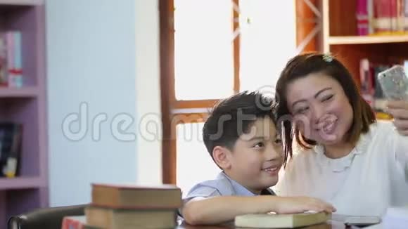 快乐的亚洲男孩和妈妈在图书馆用手机拍照视频的预览图