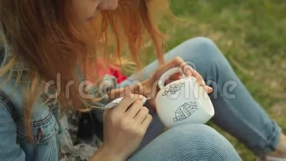 特写女性手在白色杯子上画图案女孩在晚上坐在草地上画装饰品视频的预览图