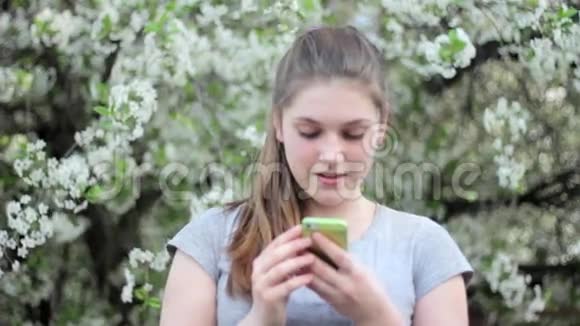公园里有智能手机的少女春天在一棵开花的树的背景下视频的预览图