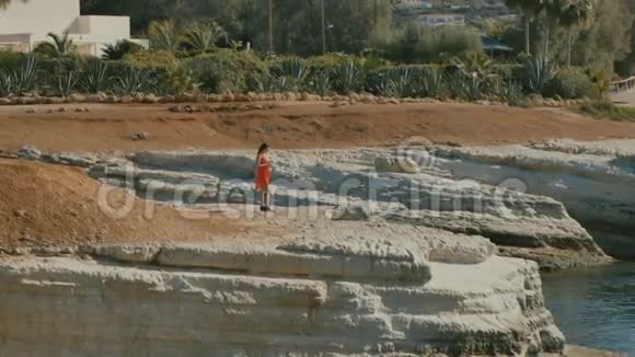 穿橙色衣服的女人在海边的岩石上视频的预览图