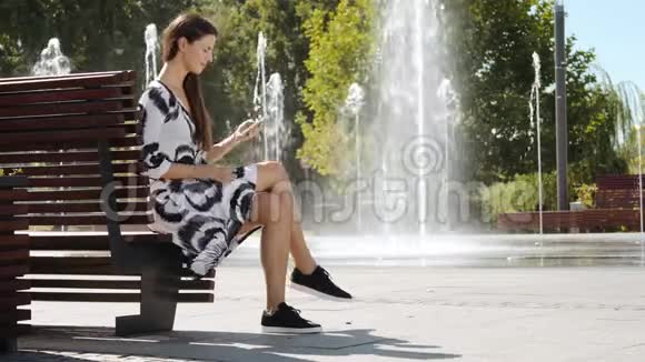 年轻的女商人穿着裙子坐在长凳上打电话视频的预览图
