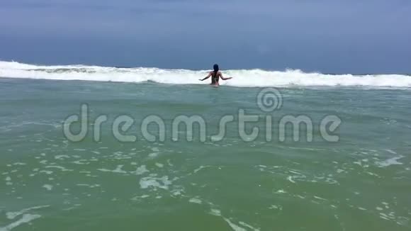 迷人的年轻女子在海浪上跳跃和玩耍视频的预览图