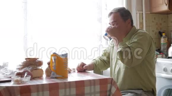 有胡子的老人端着一杯热饮和饮料他坐在窗边在家吃早饭视频的预览图