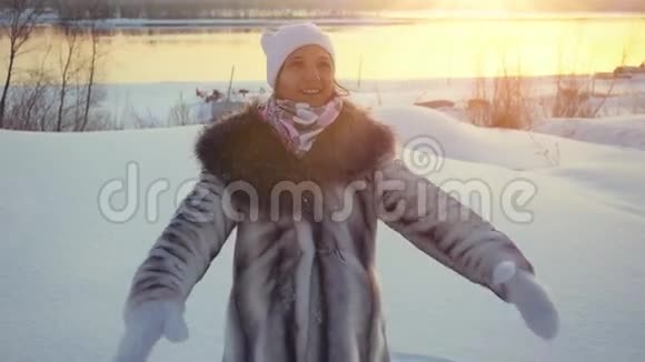 快乐的年轻美丽的女人在冬天落下来躺在雪地里在日落的时候在阳光慢慢地躺着视频的预览图