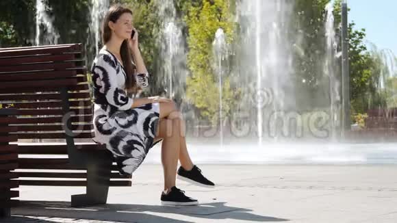 年轻的女商人穿着裙子坐在长凳上打电话视频的预览图