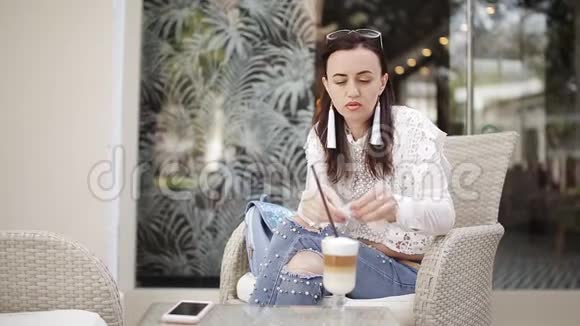 咖啡屋里的女孩坐在椅子上喝着杯子里的拿铁穿过一根稻草视频的预览图