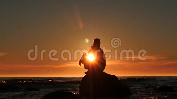 一个人在海中的岩石上剪影想着多莉在夕阳下拍摄视频的预览图