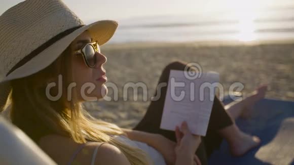 日落时分年轻的美女坐在沙滩上的椅子上看书视频的预览图