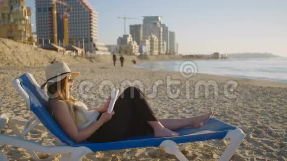 日落时分年轻的美女坐在沙滩上的椅子上看书视频的预览图