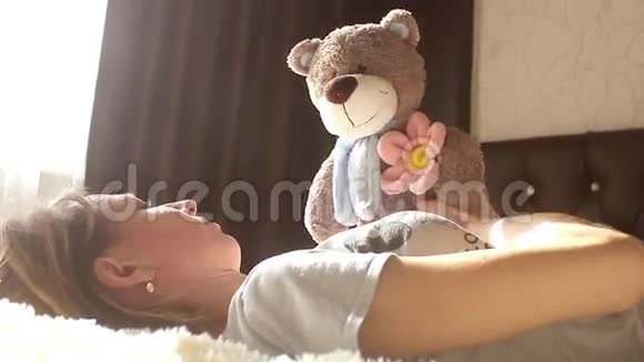 女孩在家里坐在床上玩玩具熊微笑着视频的预览图
