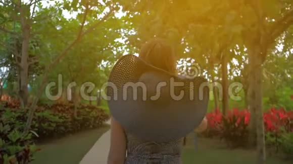 戴着蓝帽子的年轻女孩正穿过一个热带公园夏日时光视频的预览图