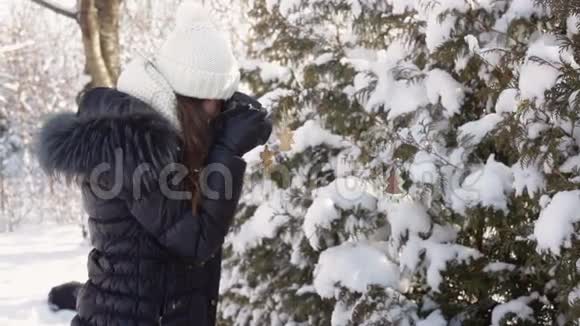 穿着冬装和针织白帽的美丽年轻女子拍摄白雪森林视频的预览图
