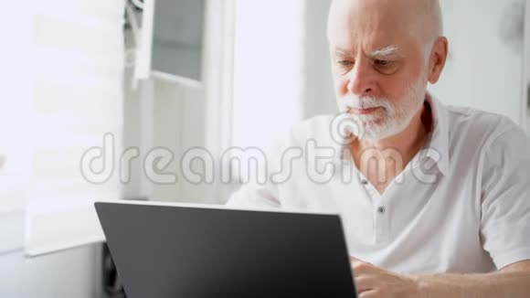 英俊的老人在家里用笔记本电脑工作退休后的远程自由职业工作视频的预览图