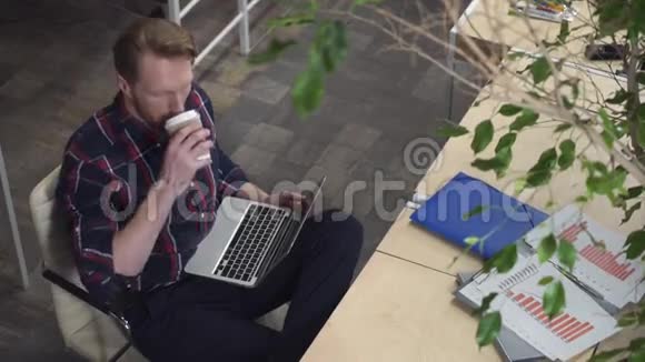 大胡子男人一边喝咖啡一边上网一边在椅子上放松视频的预览图