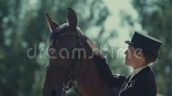 优雅的女骑手穿着一件长外套和帽子抚摸马视频的预览图