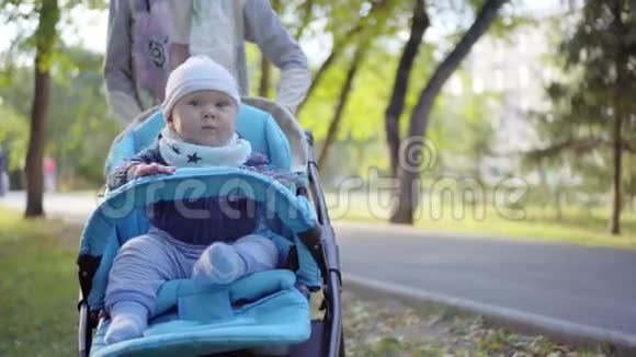 妈妈在婴儿车里卷着蹒跚学步的孩子婴儿挥舞着手臂户外活动视频的预览图