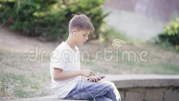 带着智能手机坐在路边听音乐的带耳机的少年视频的预览图