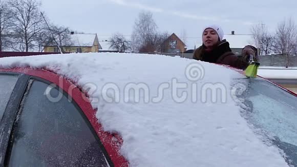 女孩在红色汽车的屋顶上擦雪冬季缓慢运动视频的预览图