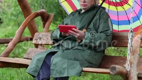带伞的女人坐在秋千凳上使用智能手机视频的预览图