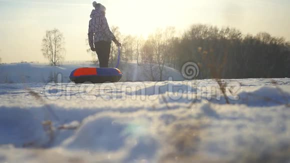 女孩在冬季公园里滑雪年轻的女人在山上背着雪橇在阳光下缓慢地运动视频的预览图
