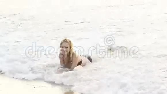 穿着泳衣的金发女孩躺在波涛中的浅海中视频的预览图