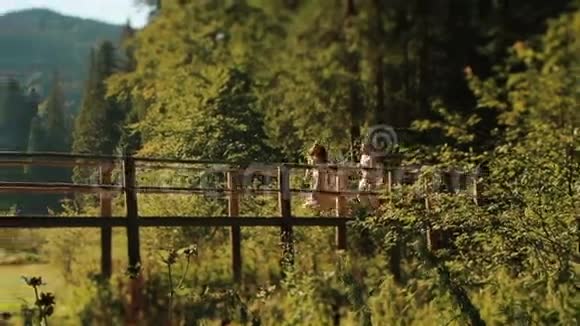 美丽的年轻幸福夫妇穿着传统的乌克兰服装在山上的木桥上散步玩得很开心视频的预览图