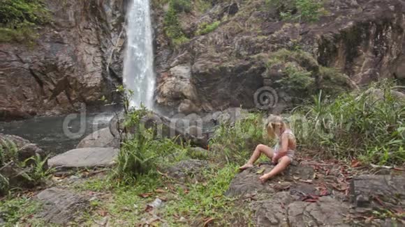 小女孩坐在石头上对抗高瀑布瀑布视频的预览图
