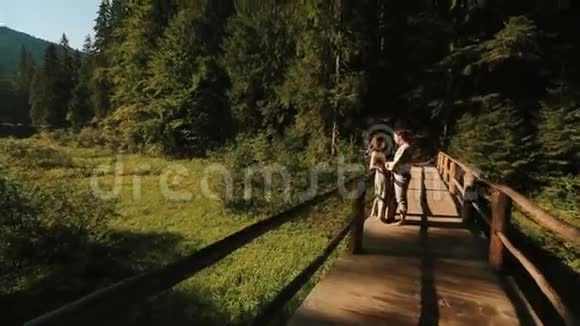 在喀尔巴阡山的木桥上穿着传统的乌克兰服装的幸福美丽的一对夫妇轻轻地接吻玩得开心视频的预览图