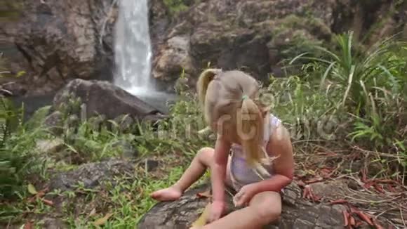 特写小女孩在石头上与瀑布级联视频的预览图