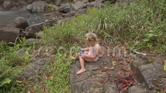 小女孩在石头上打电话对抗瀑布视频的预览图