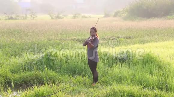 一个在草地上拉小提琴的亚洲女人视频的预览图
