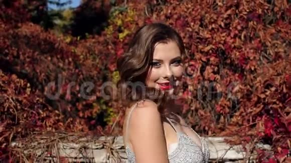 穿着漂亮晚礼服的女孩在秋天的金色公园散步视频的预览图