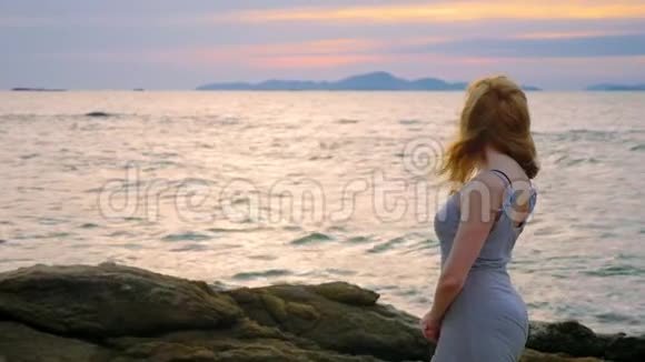 年轻女子走在岩石上欣赏日落美景溅起浪花视频的预览图